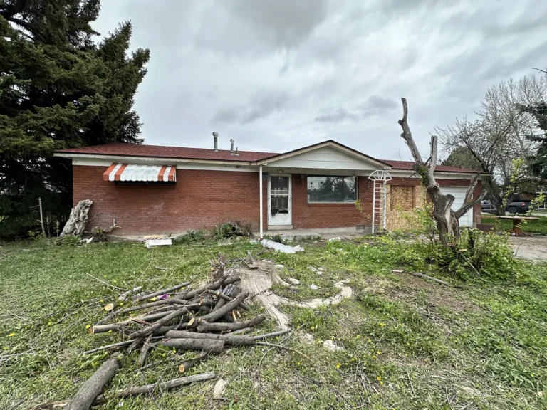 Brick ranch house with downed branches piled in the front yard