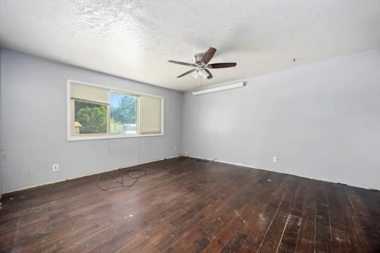 Empty living room with dark wood floors and a ceiling fan