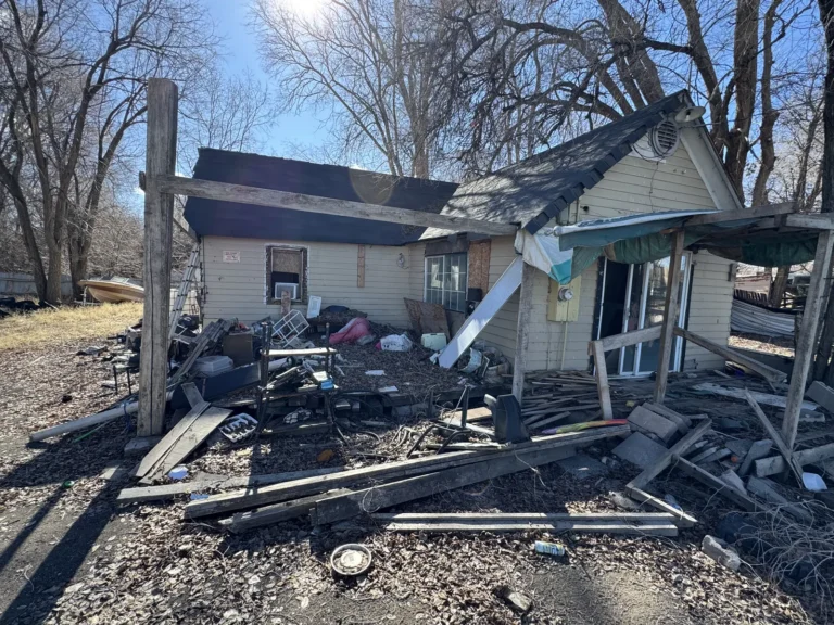 House with a collapsed porch and debris across the yard